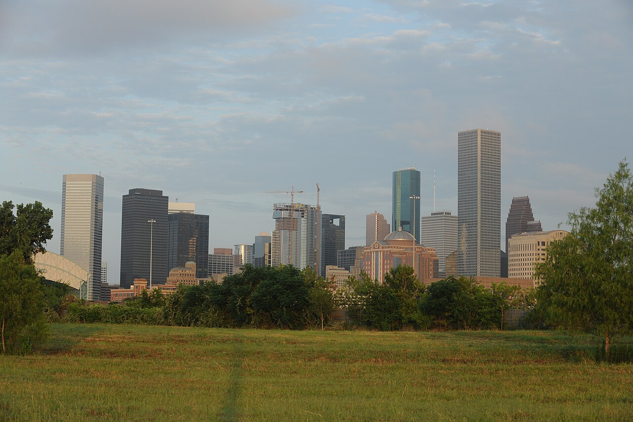 Houston downtown towers over a grassy field at sunrise