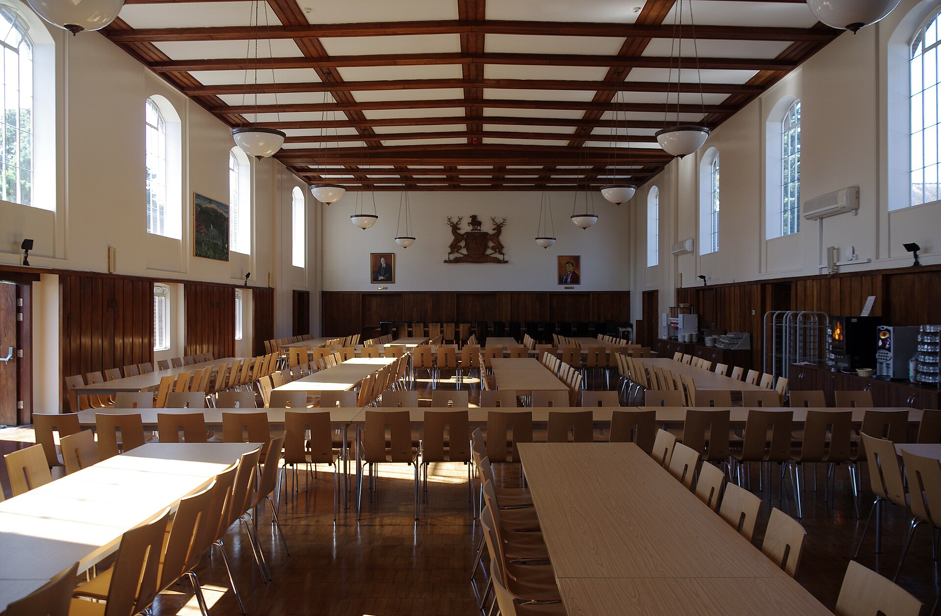 Long dining tables in an empty hall with a wood-beamed ceiling, ready for supper